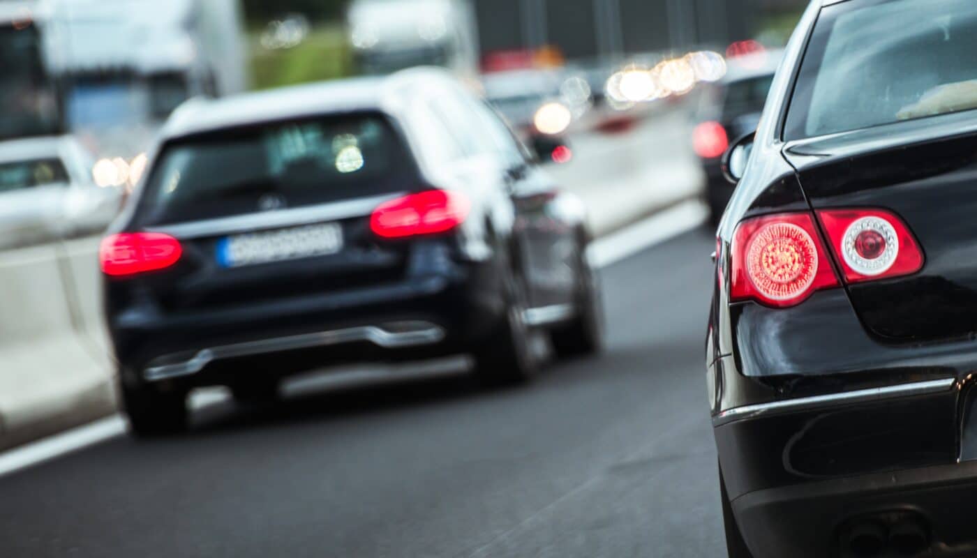 Pendlerpauschale_Rückansicht mehrerer Autos im dichten Verkehr auf einer mehrspurigen Straße, Fokus auf ein bremsendes schwarzes Auto mit leuchtenden Rücklichtern.