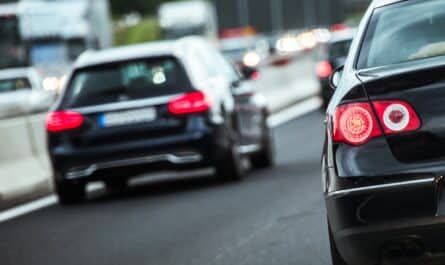 Pendlerpauschale_Rückansicht mehrerer Autos im dichten Verkehr auf einer mehrspurigen Straße, Fokus auf ein bremsendes schwarzes Auto mit leuchtenden Rücklichtern.