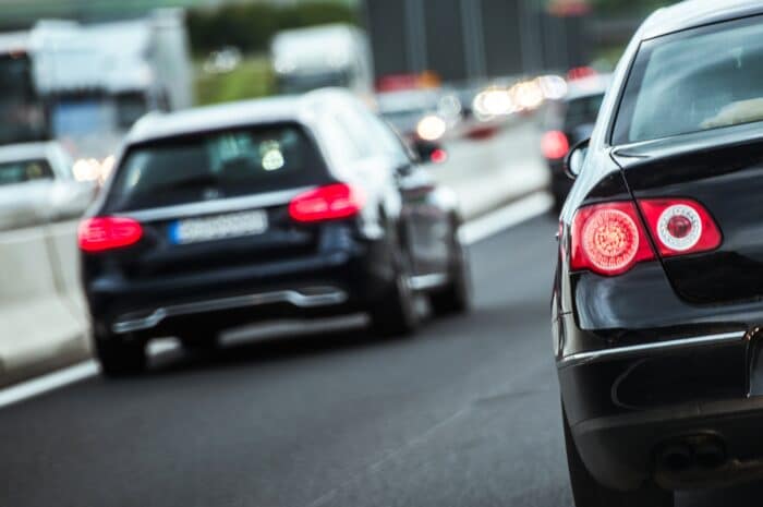 Pendlerpauschale_Rückansicht mehrerer Autos im dichten Verkehr auf einer mehrspurigen Straße, Fokus auf ein bremsendes schwarzes Auto mit leuchtenden Rücklichtern.